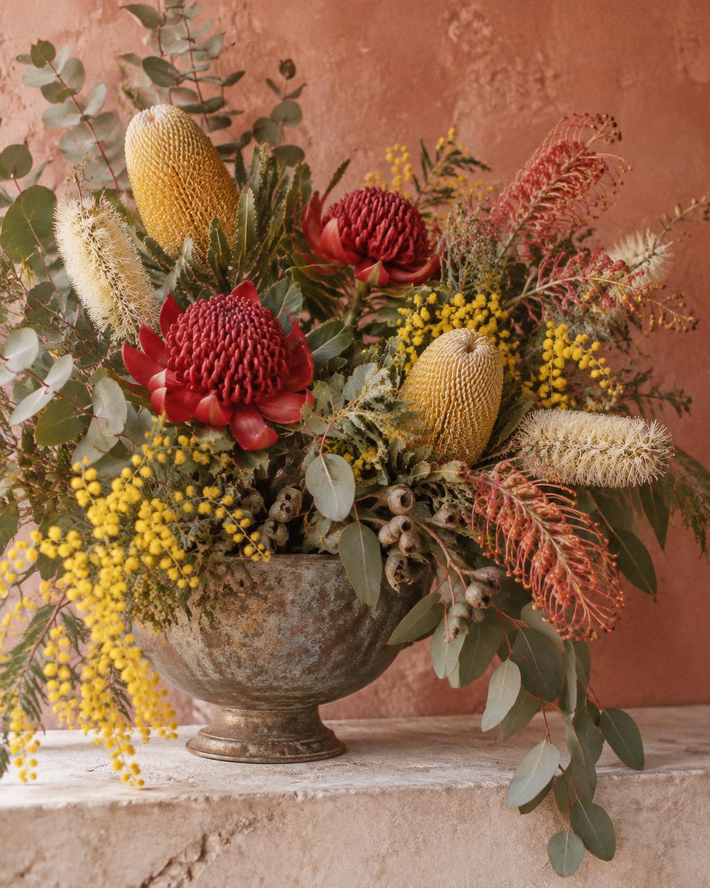 Australian native arrangement with red waratahs, yellow banksias, golden wattle and eucalyptus in an aged metal bowl